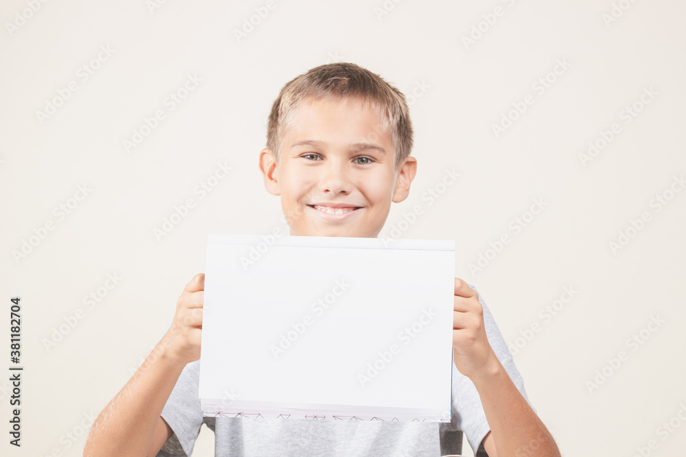 Boy holding open blank notebook over light wall background indoors Boy holding open blank notebook over light wall background indoors