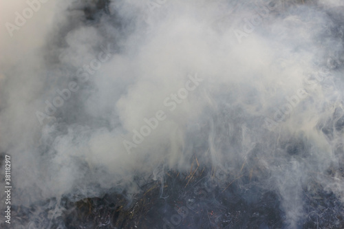 Gray smoke streaked with yellow from the fire. Background of black burnt grass and ash.