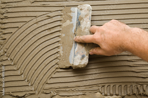Worker hand using spatula and putting glue on wall for gluing ceramic tiles. Closeup.