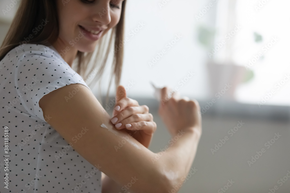 Naklejka premium Crop close up of smiling young Caucasian woman do daily beauty spa procedures or treatment at home. Happy girl apply moisturizing or nourishing body cream or lotion for healthy glowing skin.