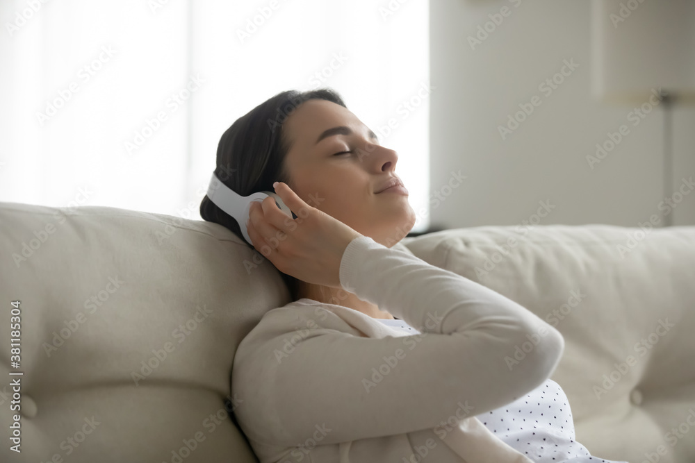 Happy millennial girl in modern wireless headphones relax on couch at home listen to music relieve negative emotions. Young woman in earphones rest dream on sofa enjoy good quality sound on gadget. Happy millennial girl in modern wireless headphones relax on couch at home listen to music relieve negative emotions. Young woman in earphones rest dream on sofa enjoy good quality sound on gadget.
