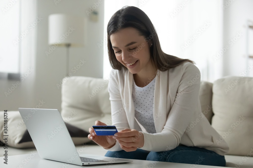 Smiling millennial Caucasian girl sit on couch at home shopping online on laptop with credit card. Happy young woman client buyer make web payment using secure internet service system on computer. Smiling millennial Caucasian girl sit on couch at home shopping online on laptop with credit card. Happy young woman client buyer make web payment using secure internet service system on computer.