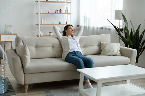 Happy millennial Caucasian girl relax on comfortable sofa in living room breathe fresh air in own home. Relaxed young woman renter rest on couch relive negative emotions. Stress free, peace concept.
