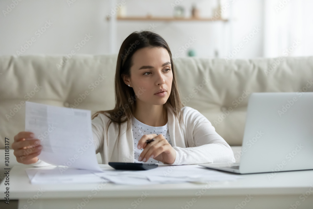 Serious young woman look at laptop screen busy managing household finances expenditures paying bills online. Pensive millennial female take care of budget count expenses, make payment on computer. Serious young woman look at laptop screen busy managing household finances expenditures paying bills online. Pensive millennial female take care of budget count expenses, make payment on computer.