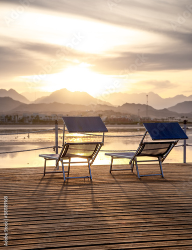 Two empty chairs on a wooden pier at sunset