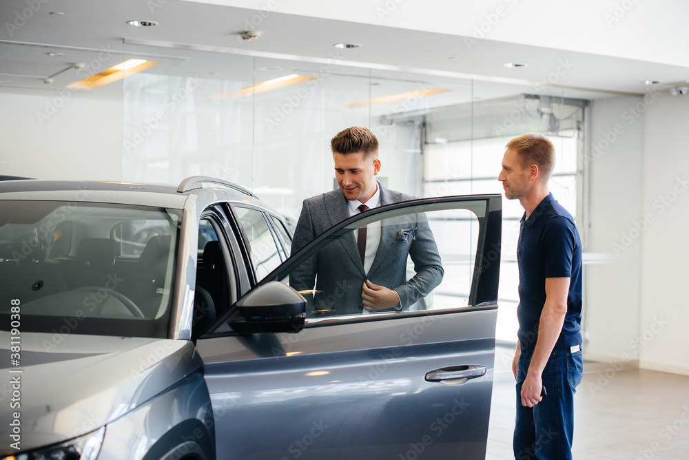 A young businessman with a salesman looks at a new car in a car dealership. Buying a car A young businessman with a salesman looks at a new car in a car dealership. Buying a car