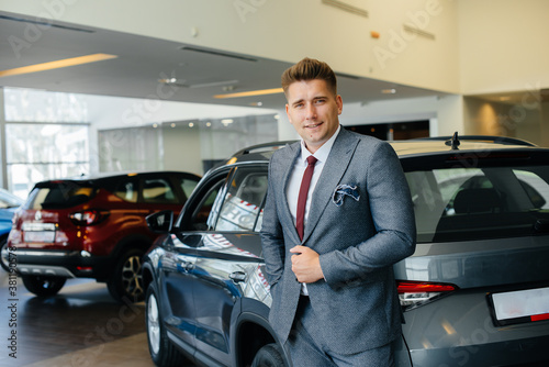 A young businessman looks at a new car in a car dealership. Buying a car © Andrii
