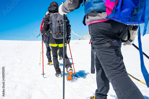 Rope team member point of view with mountaineers walking on snow and ice in sunny weather.