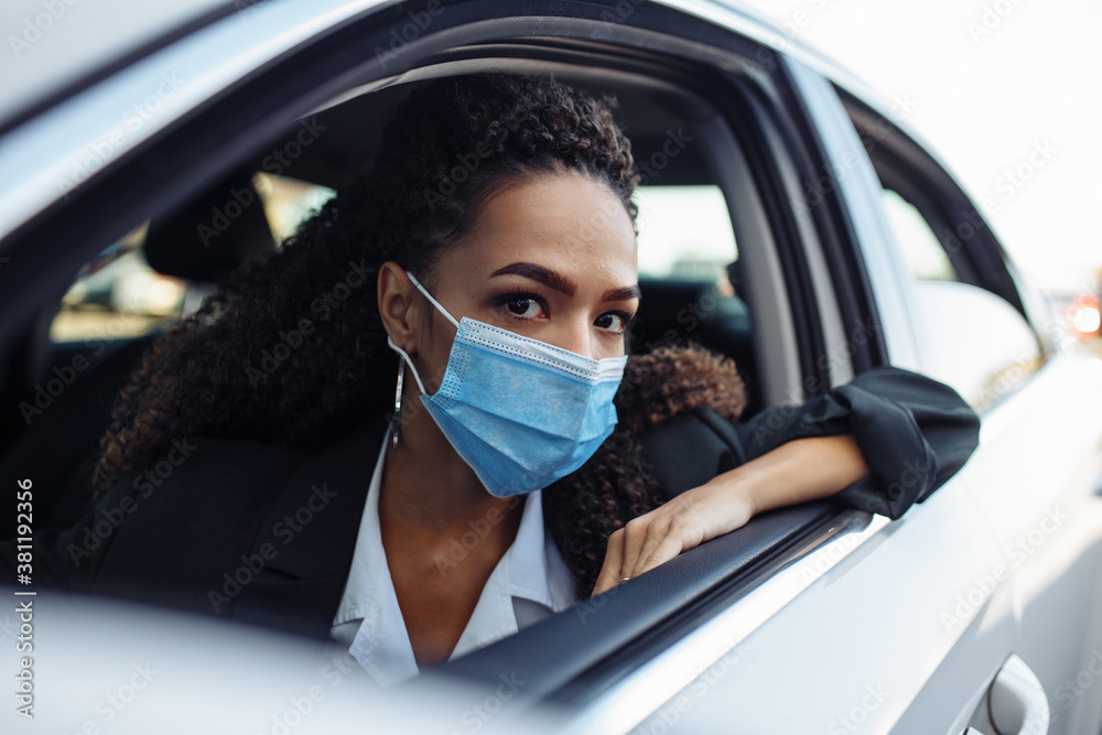 Young business woman looks out of a window of her personal car during pandemic covid-19. Business trips during pandemic, new normal and coronavirus travel safety concept.