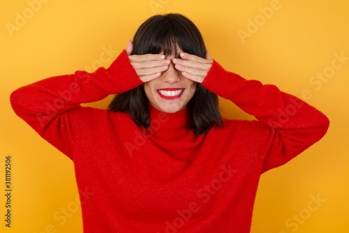 Caucasian brunette woman wearing red casual sweater isolated over yellow background covering eyes with hands smiling cheerful and funny. Blind concept. © Roquillo