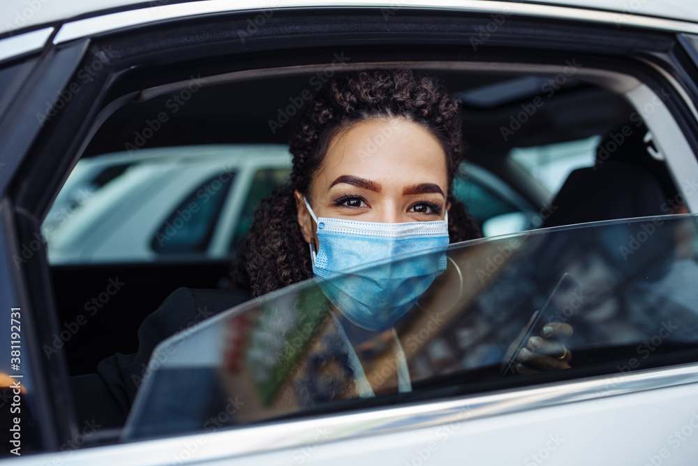 Young business woman passenger wearing a medical mask looks out of a taxi car window. Business trips during pandemic, new normal and coronavirus travel safety concept. Young business woman passenger wearing a medical mask looks out of a taxi car window. Business trips during pandemic, new normal and coronavirus travel safety concept.