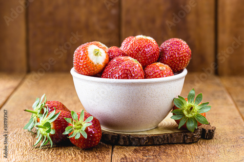 organic and fresh strawberries in recycled plastic bowl on rustic wooden background with space for text photo