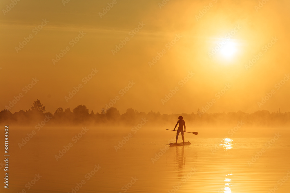 Silhouette of muscular guy training on sup board at lake
