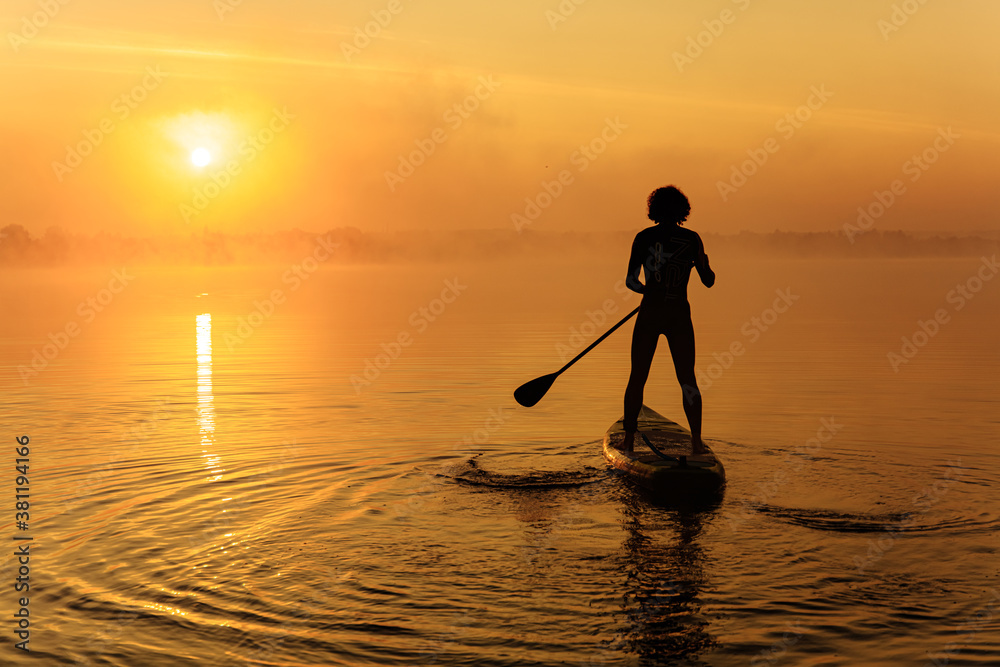 Silhouette of man floating on sup board on foggy lake