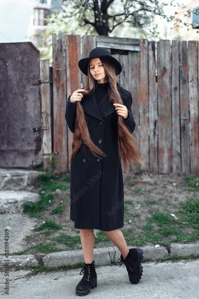 Young beautiful fashionable woman in black hat with long hair posing on woody background