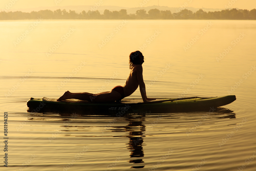 Active young guy in silhouette stretching body on sup board