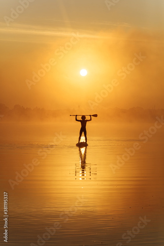 Silhouette of strong man paddling on sup board at foggy lake
