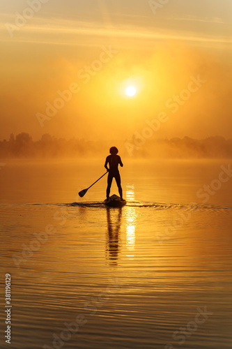 Silhouette of man swimming on sup board in early morning
