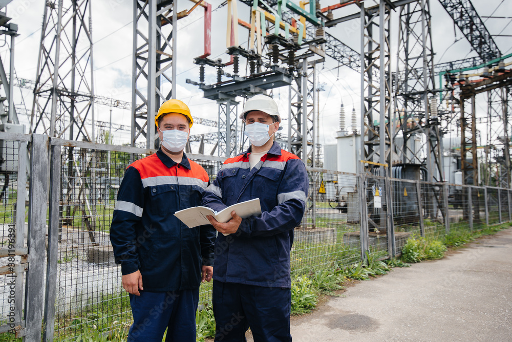 Engineers electrical substations conduct a survey of modern high-voltage equipment in the mask at the time of pandemia. Energy. Industry Engineers electrical substations conduct a survey of modern high-voltage equipment in the mask at the time of pandemia. Energy. Industry