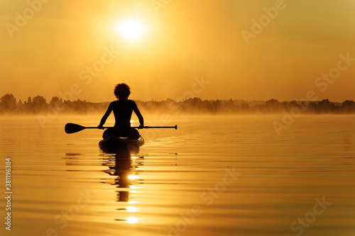 Sporty young man sitting on sup board with long paddle