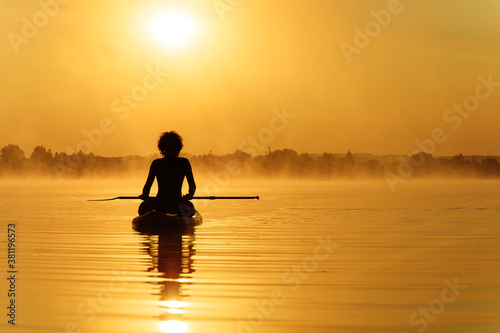Man sitting on paddle board and enjoying amazing sunrise
