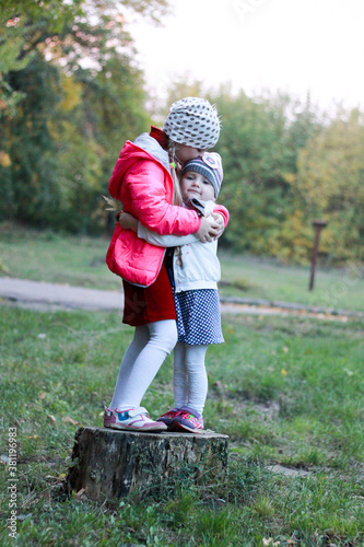 two sisters stand on a tree stump, hug and kiss