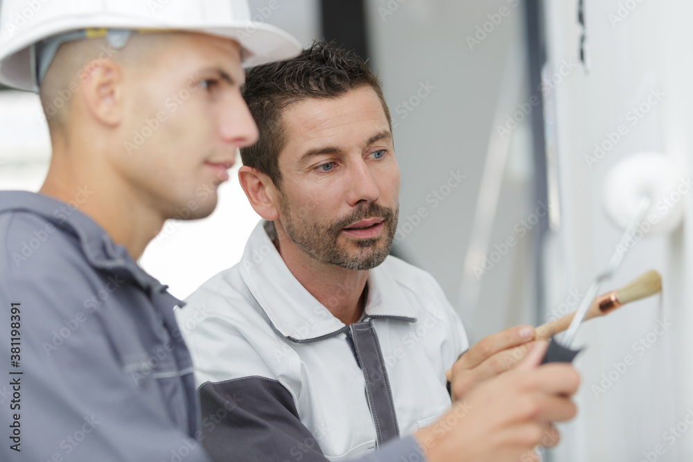 Fototapeta premium supervisor watching apprentice painter use a roller