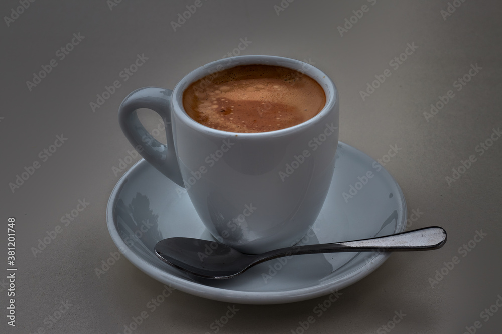 Fototapeta premium Delicious coffee in a white porcelain cup, with saucer and teaspoon