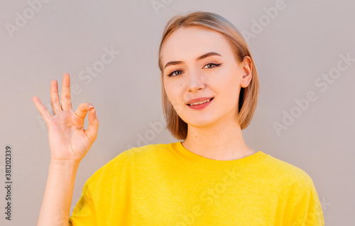 Young cute smiling girl showing OK sign on gray