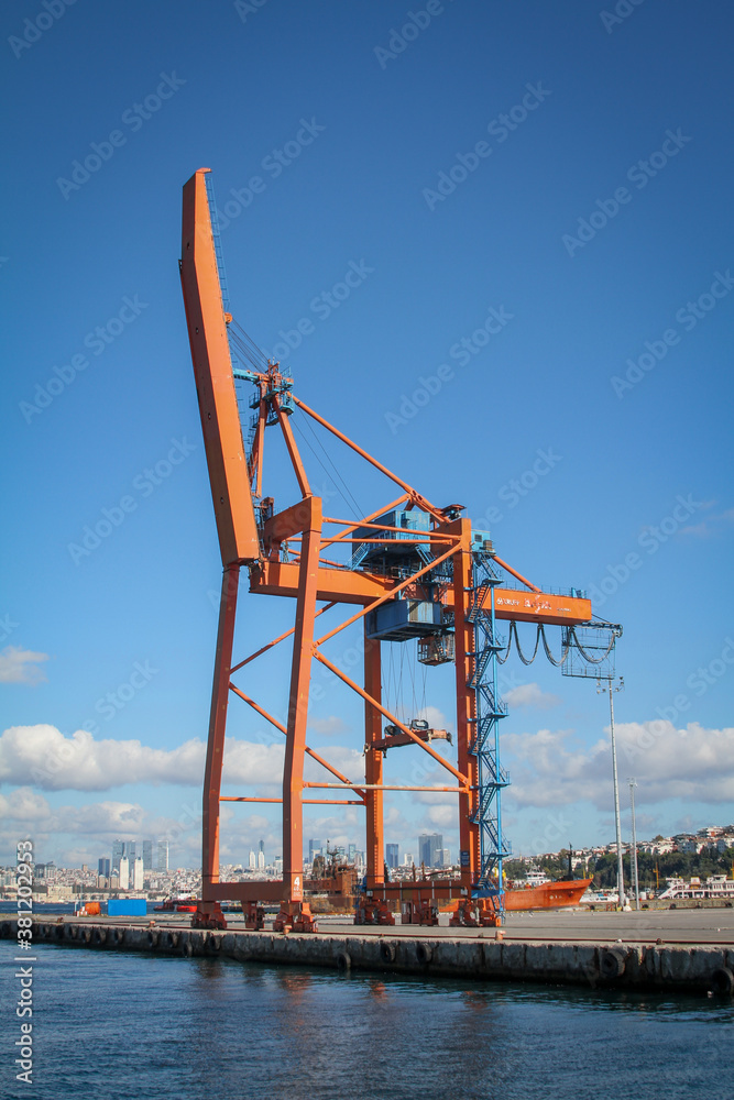 Huge orange crane in a harbour, blue sky, few clouds.