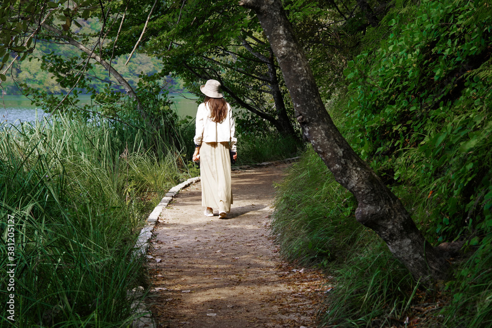 Fototapeta premium Young woman traveler walking on wooden path trail in Plitvice Lakes National Park, UNESCO natural world heritage and famous travel destination of Croatia
