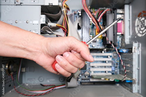 A hand of a technician repairer holding a screwdriver in order to upgrade or repair a broken home computer