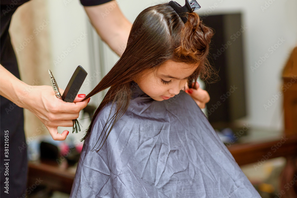 Naklejka premium Little Girl Having Her Hair Cut. Little Girl Sitting In Beauty Hair Salon Style For Children.