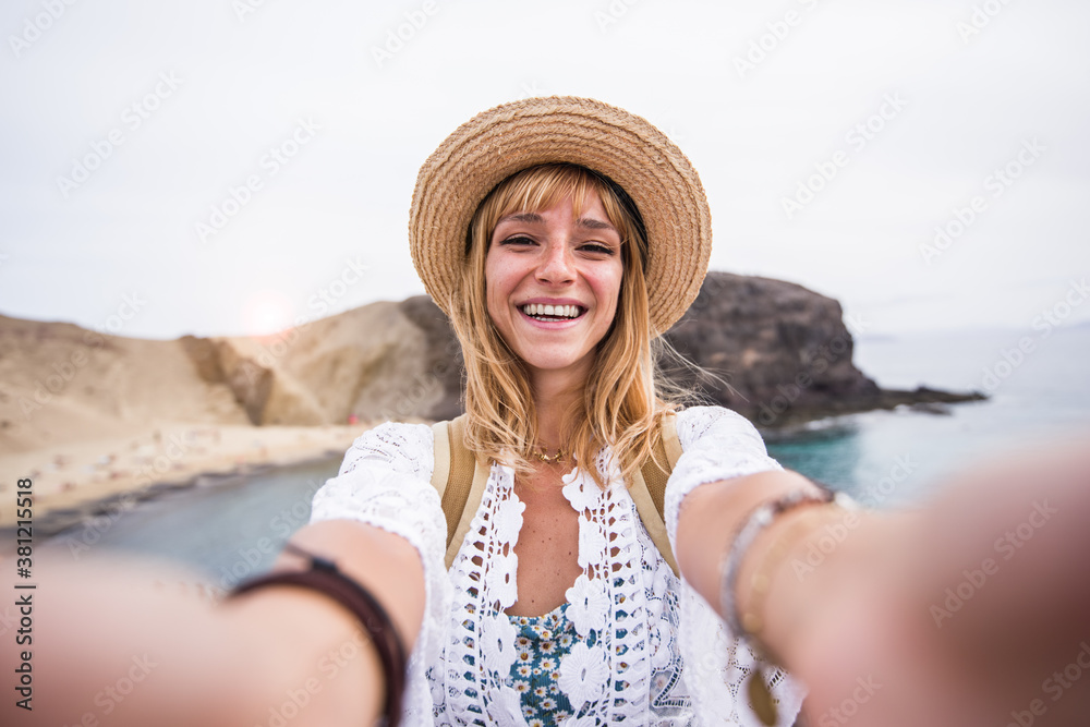 Beautiul young woman with hat taking a selfie at the beach. Happy portrait of a caucasian girl smiling at the camera outdoor.