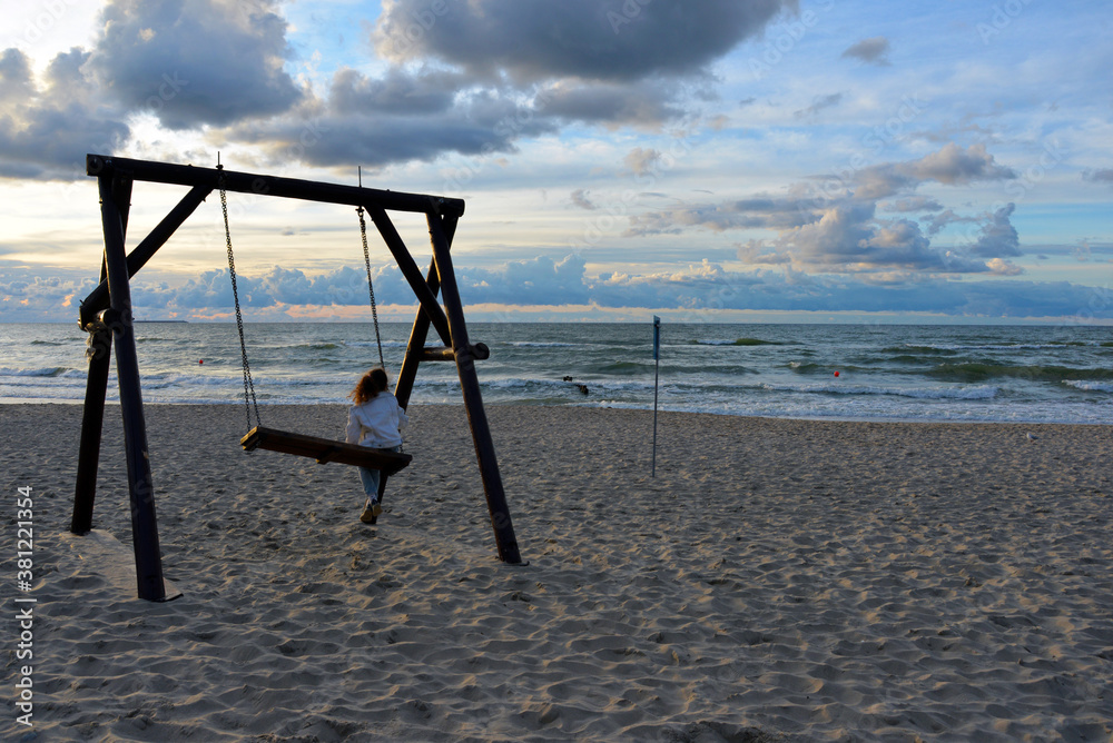 a little girl rides on a wooden swing against the background of the waves of the Baltic sea and the beautiful sky. a little girl rides on a wooden swing against the background of the waves of the Baltic sea and the beautiful sky.