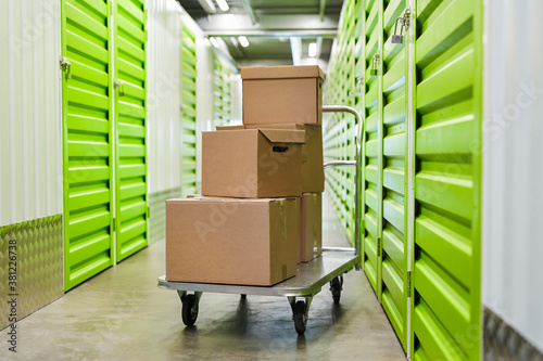 Background image of cart with cardboard boxes in empty hall of self storage facility, copy space photo