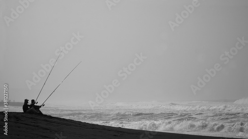 Silhouette of two men fishing by the sea. Sitting alone holding the long fishing rod.