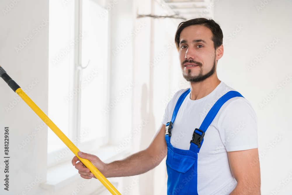 Medium shot, construction worker in blue work clothes paints wall in apartment Medium shot, construction worker in blue work clothes paints wall in apartment