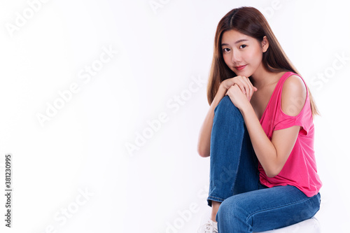 Joyful young woman with long hair wear pink t-shirt showing palm hand while sitting on chair over isolated against white background.