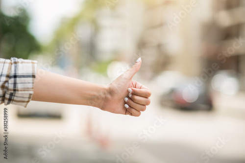 Hitchhiker. Woman hand showing thumbs up to travel in urban city. Holiday travel trips concept. photo