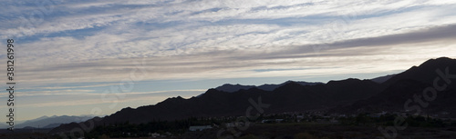 Sunset in the Andes mountains. Panorama view of the sun hiding behind the dark mountains silhouette at dusk.