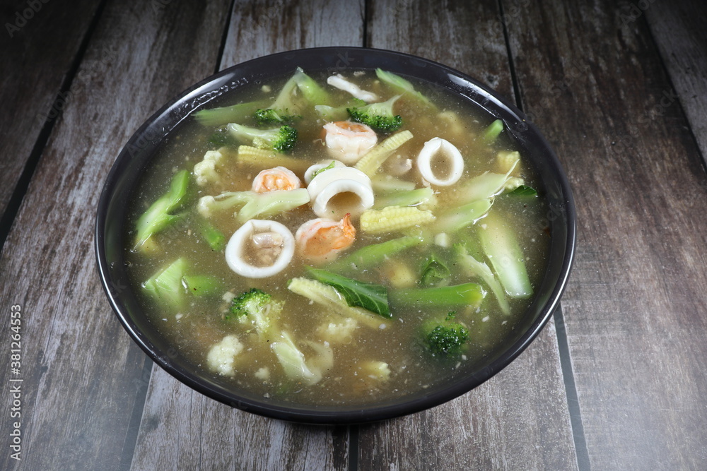 Gravy soup of Chinese kale, sliced squid, fresh peeled shrimp and cutting chicken seasoning with pepper in the bowl. Famous hot soup topping with fried noodle in Asia restaurant. Gravy soup of Chinese kale, sliced squid, fresh peeled shrimp and cutting chicken seasoning with pepper in the bowl. Famous hot soup topping with fried noodle in Asia restaurant.