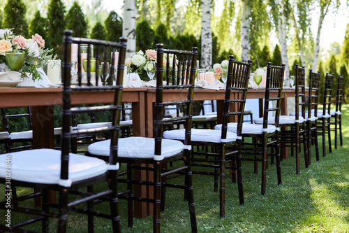 chairs and dinner tables with white cloth, served with porcelain and green glasses. Georgeous wedding table decorated with flowers on a green lawn