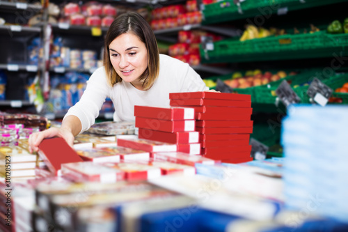 attentive girl customer looking for tasty sweets on shelves in supermarket