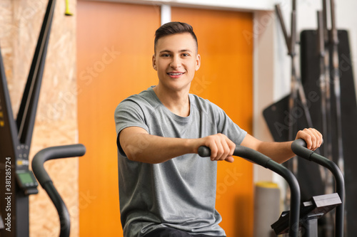 Young man training on exercising bike in gym