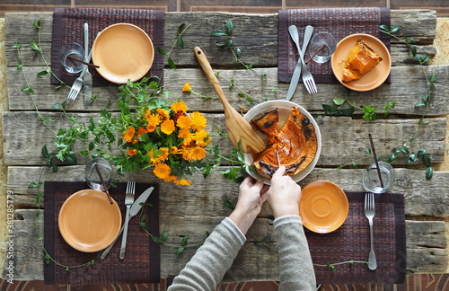 Thanksgiving wooden ancient table setting process. Hostess hands lay pumpkin on plates. Rustic style.