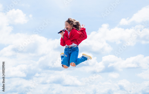 teen kid jumping and singing with microphone in karaoke. child singing outdoor. singer with microphone. happy childhood. happy girl enjoy the moment. Have Fun on Celebration © be free