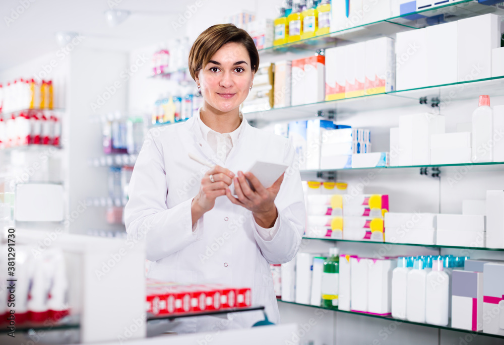 Young girl pharmacist is writing down assortment of drugs in pharmacy.