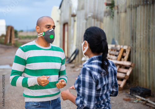Two latino farm workers in face masks talking outdoors near glasshouse, consulting and discussing © JackF
