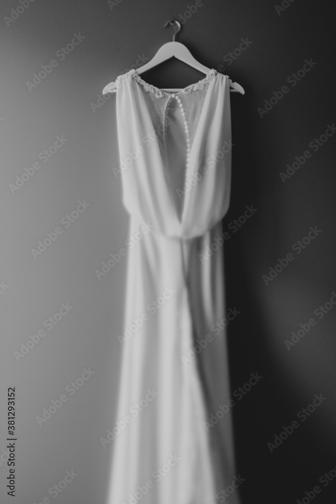 White wedding dress of the bride with a cutout on the back on a hanger on a nail with a shallow depth of field.